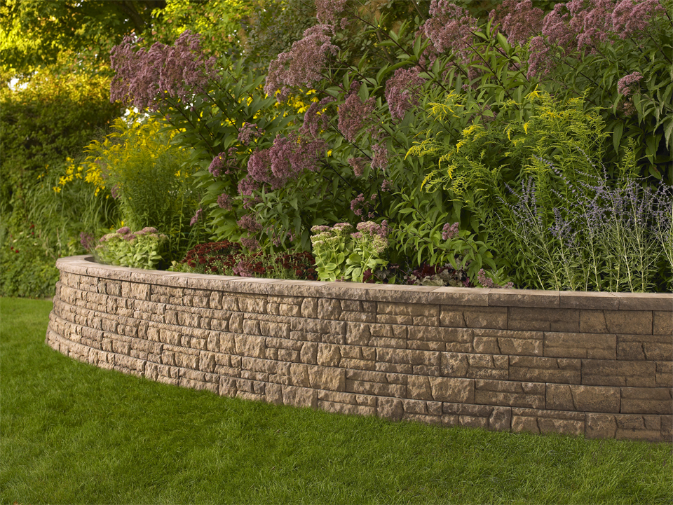 Curved high walled raised Flores concrete retaining wall planter with red, pink, and purple flowers surrounded by green grass