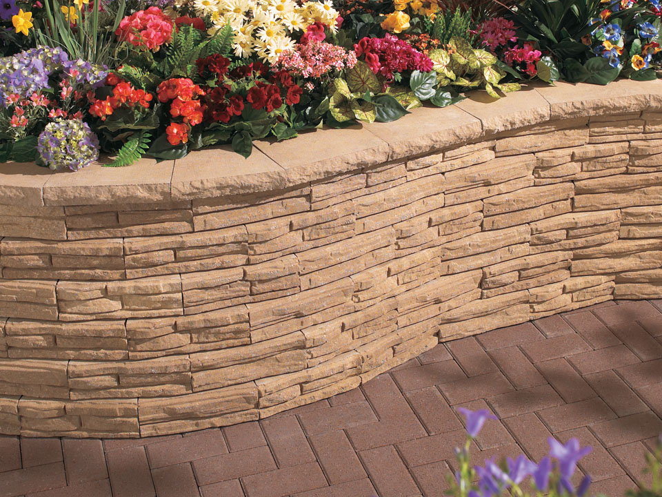 Close view of curved raised Natural Impressions Flagstone concrete block retaining wall planter on a paver patio. 