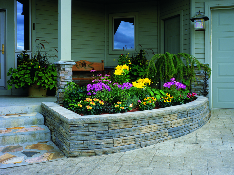 Green front porch with stone steps and a curved raised Natural Impressions Flagstone concrete block planter. 